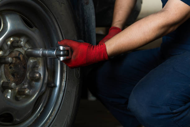 Low down view of a mechanic engineer using a socket wrench to remove wheel bolts from a vehicle stock photo