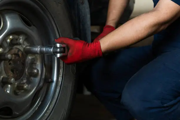Photo of Low down view of a mechanic engineer using a socket wrench to remove wheel bolts from a vehicle