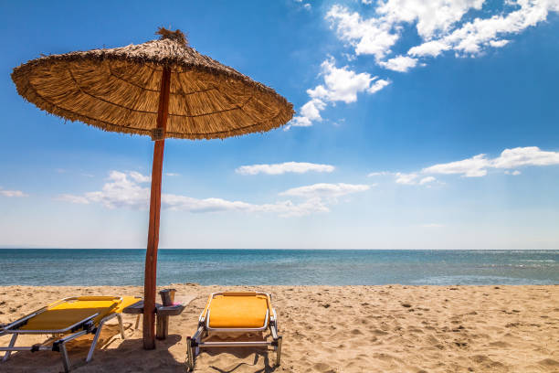 A straw umbrella with deck chairs on a sandy beach by the sea. A straw umbrella with deck chairs on a sandy beach by the sea. The Paralia, a tourist seaside part of the municipality Katerini, Greece, Europe. katerini greece photos stock pictures, royalty-free photos & images