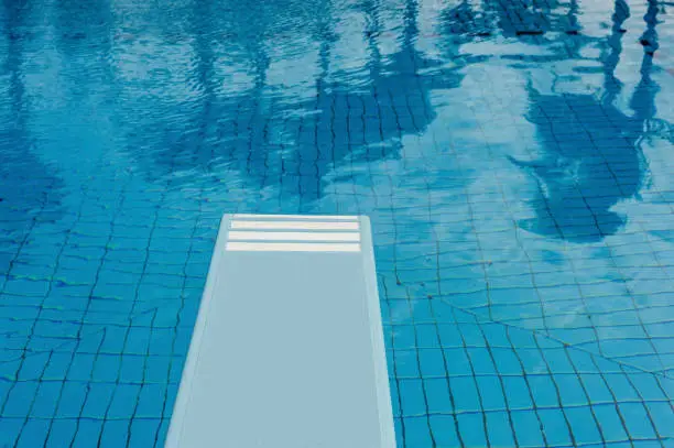 Crystal clear swimming pool with refreshing blue water, springboard and reflection of trees