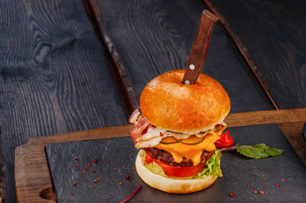 istock Juicy hamburger with ham, beef and cheddar cheese on rustic wooden board with knife 1137511811