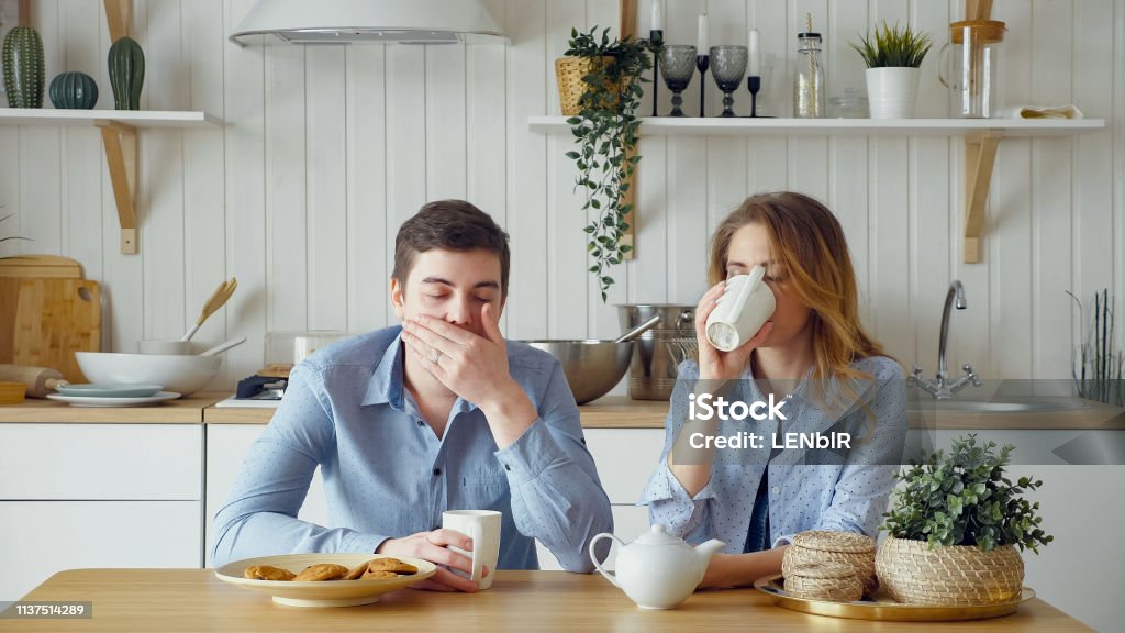 sad couple girl guy have breakfast drinking tea silently sad couple blonde girl and guy have breakfast drinking tea with biscuits silently and man yawns at table in kitchen, Breakfast Stock Photo