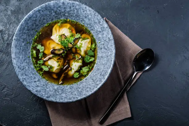 Photo of soup wonton chicken broth with mushrooms and herbs, dark background