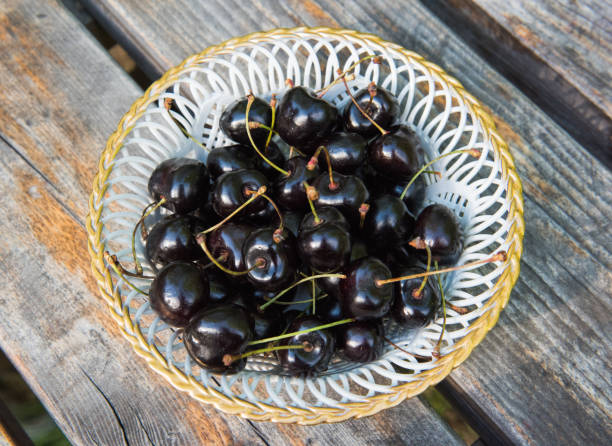 White plate of ripe black cherries with on a wooden table stock photo