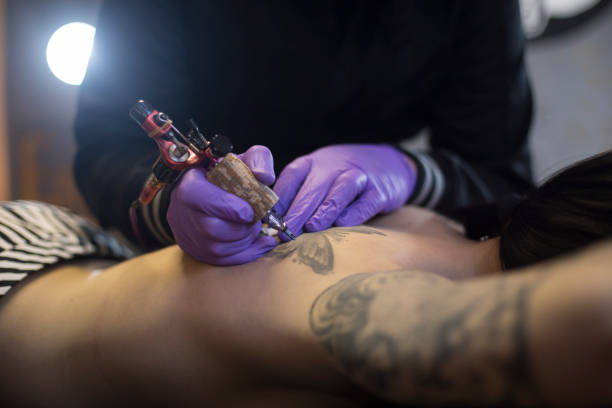 Tattooing Unrecognizable Caucasian young woman is getting a tattoo on her shoulder. back shoulder tattoos for women pictures stock pictures, royalty-free photos & images