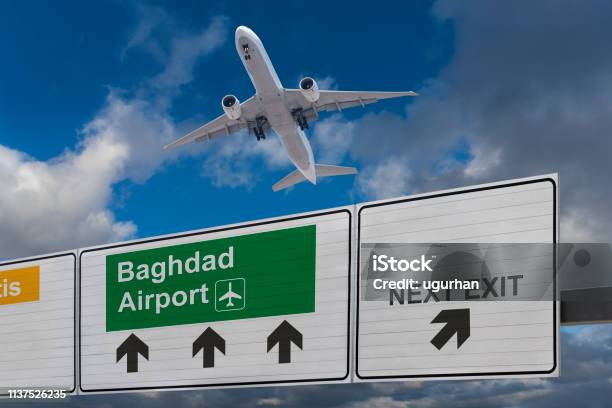 Road Sign Indicating The Direction Of Baghdad Airport And A Plane That Just Got Up Stock Photo - Download Image Now