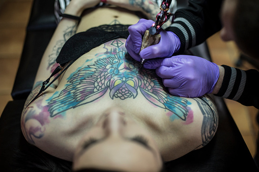 Queer tattoo artist tattooing a client