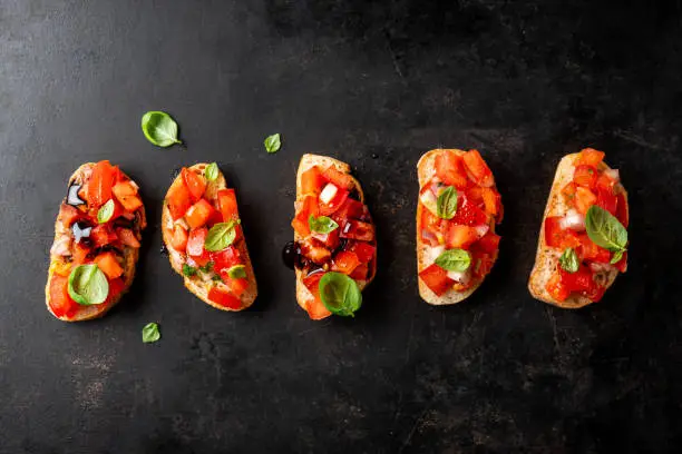 Bruschetta with tomatoes, onion, olive oil and basil on dark background. Closeup.