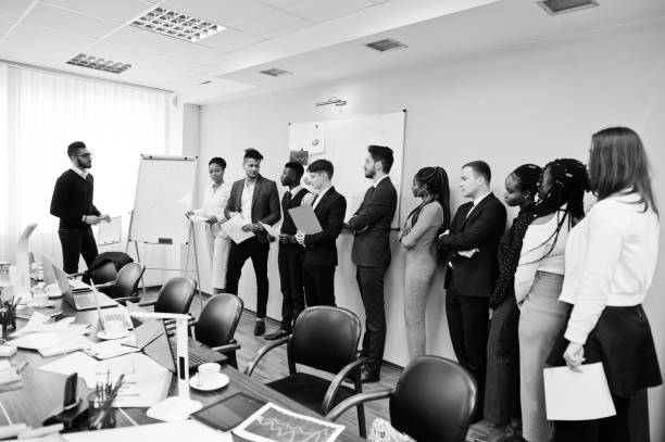 istock Mixed race business coach presenting report standing near whiteboard pointing on sales statistic shown on diagram and chart teach diverse company members gathered together in conference room. 1137533558
