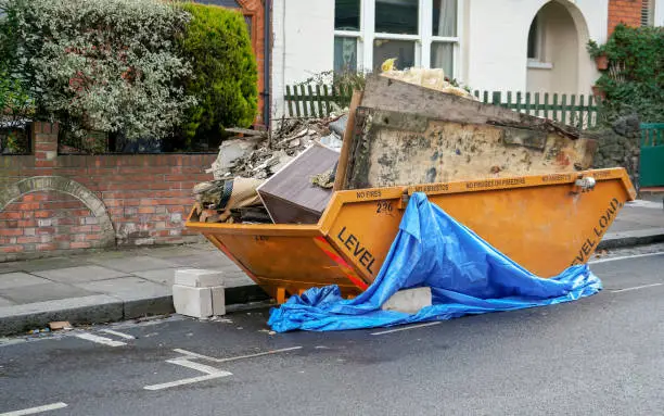 Large orange metal skip container in front house, full of rubbish from household reconstruction
