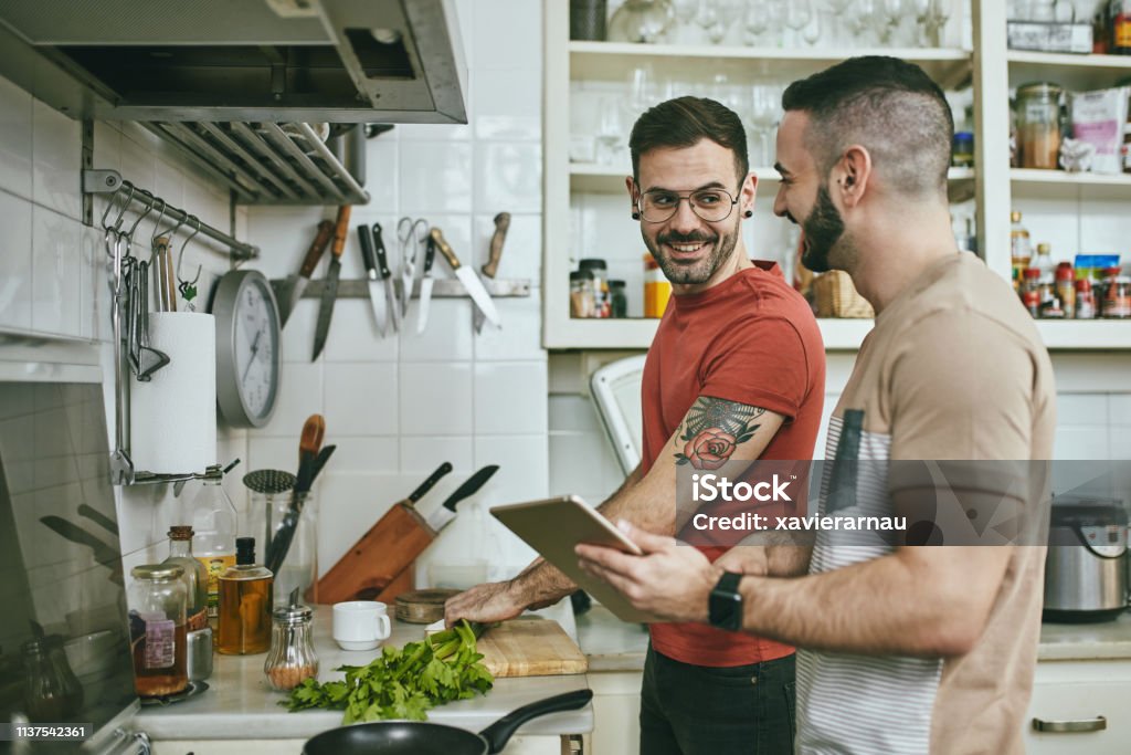 Man talking with boyfriend while preparing food Gay man talking with boyfriend while chopping vegetable at counter. Happy homosexual couple is standing in kitchen. They are spending weekend at home. Cooking Stock Photo