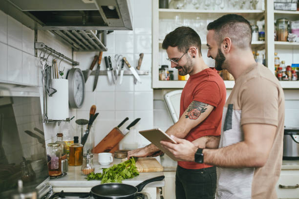 mann steht bei einem freund, der zu hause essen zubereitet - standing digital tablet couple love stock-fotos und bilder