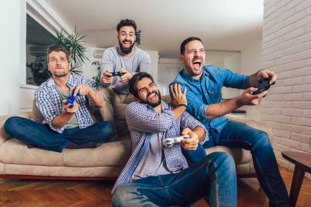 amigos masculinos sonriendo jugando videojuegos en casa y divirtiéndose. - espacio masculino fotografías e imágenes de stock