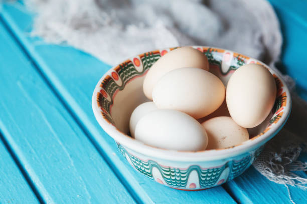 Raw eggs lie in a plate on a wooden blue table.