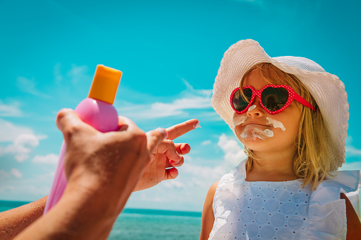 sun protection - mom put suncream on little girl face at beach vacation