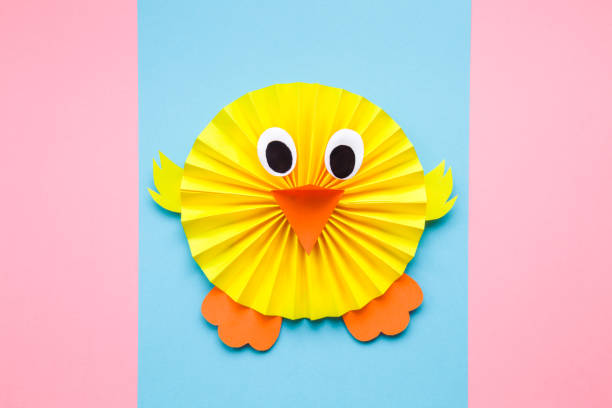 istock Happy yellow chick folded and created from paper on pastel blue and pink background. Top view. 1137553862