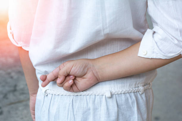 pesce d'aprile.primo passo della mano della bambina che incrocia le dita dietro la schiena. l'indice della bambina e il dito medio si incrociano, mentono e concetto di imbroglio nel tono vintage della seppia. - fingers crossed liar dishonesty truth foto e immagini stock