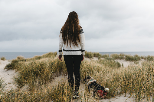 Woman and dog walking on sand dune beach on Texel island
