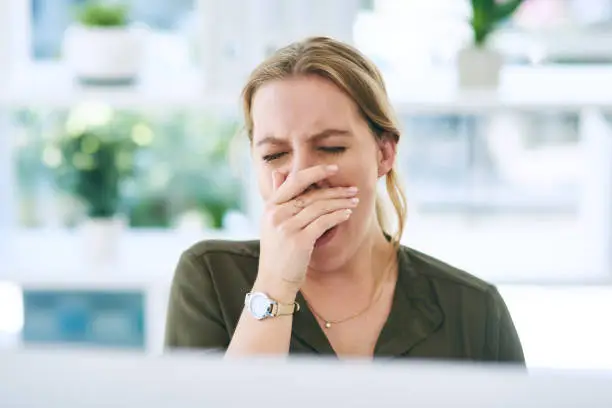 Shot of a young businesswoman yawning at her desk in a modern office
