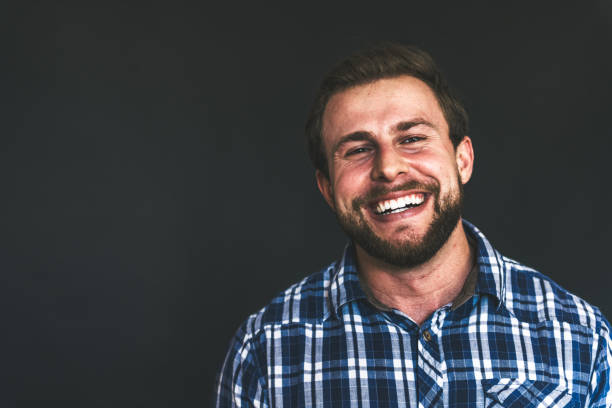 studio shot of happy young strong smiling bearded man on black background
