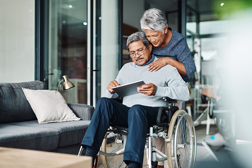Cropped shot of a cheerful elderly woman pushing her husband around in a wheelchair while he browses on a digital tablet at home during the day