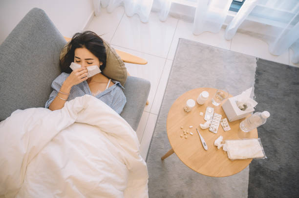 an asian chinese female lying on living room sofa covering her nose with tissue - tissue box flu virus kleenex imagens e fotografias de stock