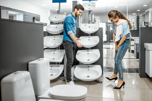 Young couple choosing new bathroom sink at the plumbing shop with lots of sanitary goods