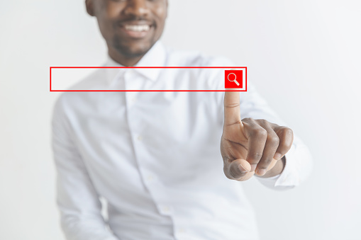 Handsome businessman pointing his finger to the camera and slicking virtual button, finger is in focus while his face is out of focus. Shallow depth of field. Young african american guy interacts with empty search bar. Negative space to insert your text.