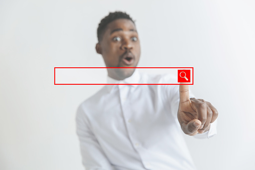 Handsome businessman pointing his finger to the camera and slicking virtual button, finger is in focus while his face is out of focus. Shallow depth of field. Young african american guy interacts with empty search bar. Negative space to insert your text.