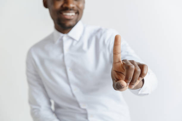 Young african american guy interacts with empty space. Negative space to insert your text or image. Handsome businessman pointing his finger to the camera and slicking virtual image or text, finger is in focus while his face is out of focus. Shallow depth of field. Young african american guy interacts with empty space. Negative space to insert your text or image. deep pick stock pictures, royalty-free photos & images