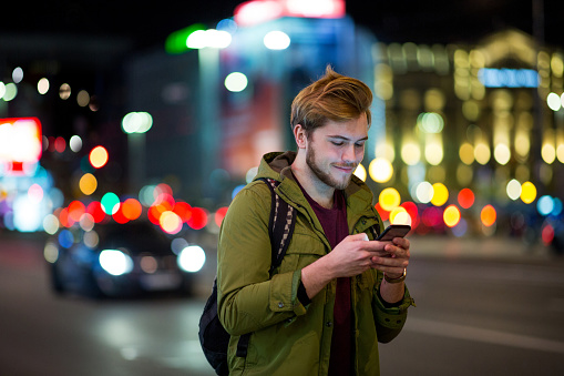 Young man using smartphone on urban street at night