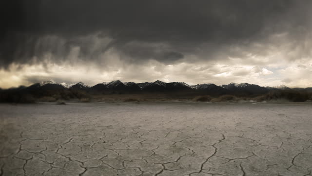 Gloomy storm, cracked lake bed in front of mountain  background.