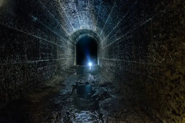 Dark and creepy old historical vaulted flooded underground drainage tunnel.