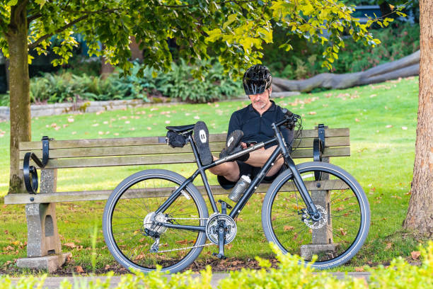 homem caucasiano assentado no banco de parque usando o smartphone - cycling shorts - fotografias e filmes do acervo