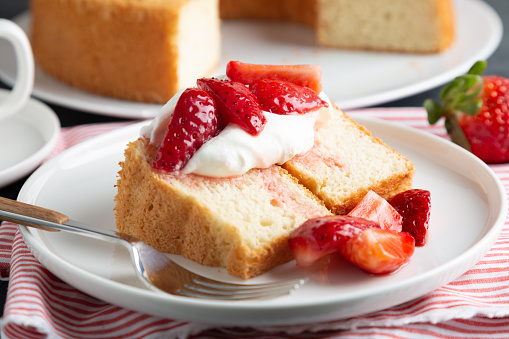 Portion of angel food cake served with whipped cream and strawberries