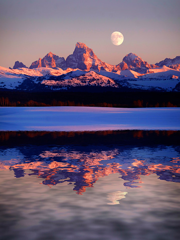 Sunset light with alpen glow on Tetons Tetons mountains rugged with moon rising reflection in water lake pond