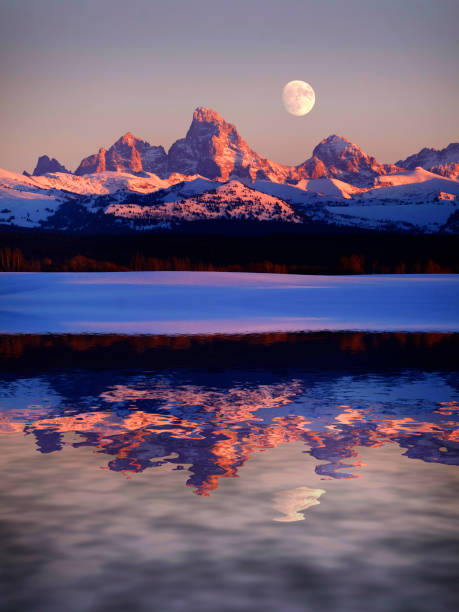 Sunset light with alpen glow on Tetons Tetons mountains rugged with moon rising reflection in water lake pond Sunset light with alpen glow on Tetons Tetons mountains rugged with moon rising reflection in water lake pond teton range photos stock pictures, royalty-free photos & images