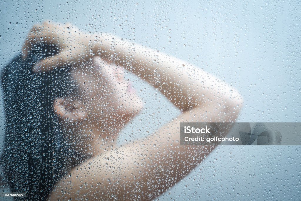 Women talking a shower behind glass windows in the shower room Women showering in the shower room close up with a water drop on glass door. Shower Stock Photo