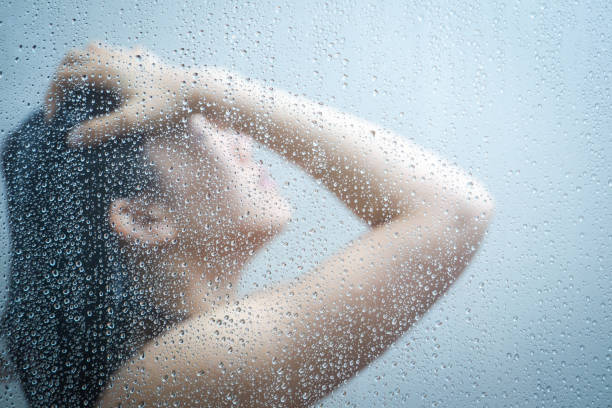 Women talking a shower behind glass windows in the shower room Women showering in the shower room close up with a water drop on glass door. woman hot shower stock pictures, royalty-free photos & images