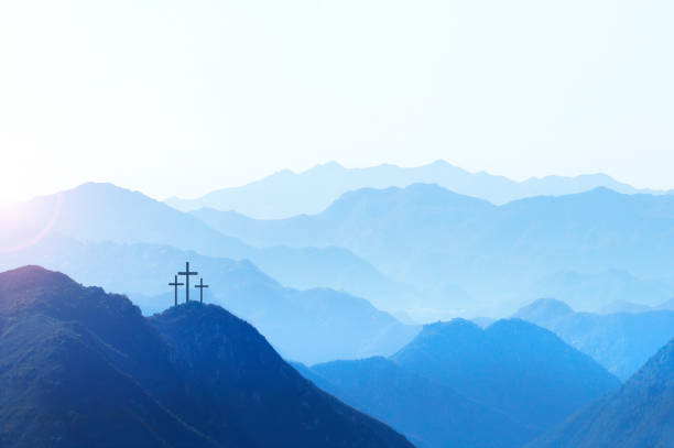 Three crosses on a hill at sunrise symbolize the Crucifixion of Christ as the sun rises in the distance. A series of mountain ridges disappear into the horizon