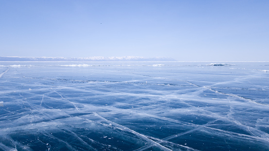 Panoramic view of the endless ice of lake Baikal in winter. Deep cracks on the surface of bright blue ice. Sunny clear weather in frosty Siberia.