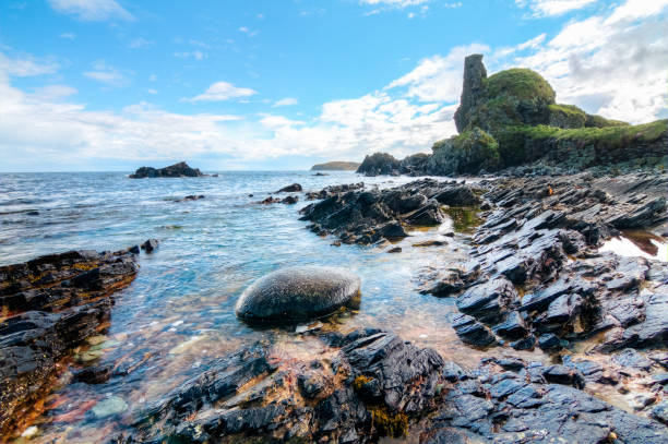 Jagged rock layers and boulders smoothed by the ocean are seen at an intertidal zone on the island of Islay, Scotland, UK.
