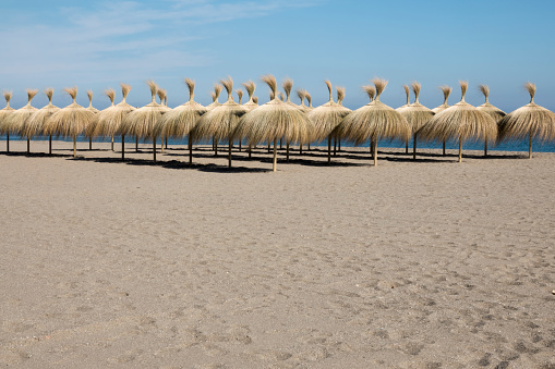 Rows of grass umbrellas on a resort beach. Sand in the foreground and copy space for your text message or promotional content.