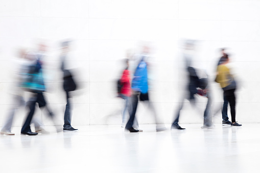 Large group of motion blurred people walking in modern hallway, London