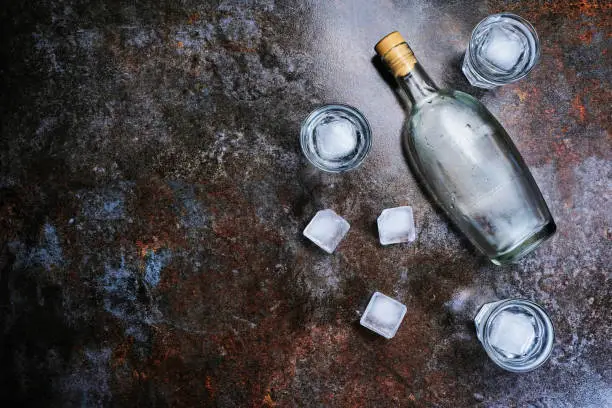 Bottle of vodka with shot glasses. On stone background. Copyspace.