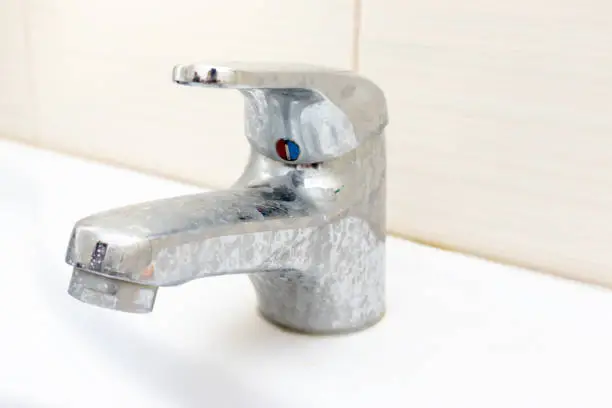 Dirty faucet with limescale, calcified water tap with lime scale on washbowl in bathroom.