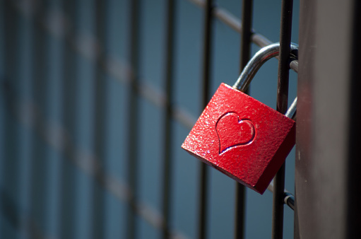 closeup of love padlock on metallic fence on blurred water background