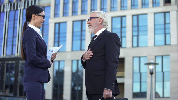 elderly male in business suit meeting young female partner near office center - aging process middle women men imagens e fotografias de stock