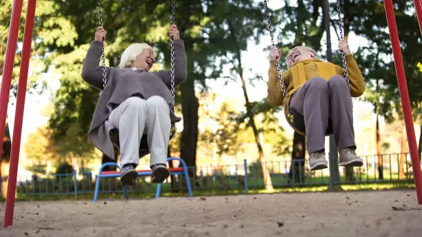 Two elderly women laughing riding swings in park, elderly friends, retirement