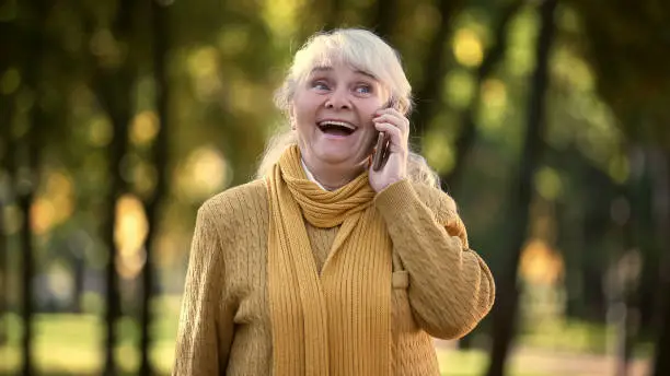 Smiling old woman talking on mobile phone in park, full family and friends